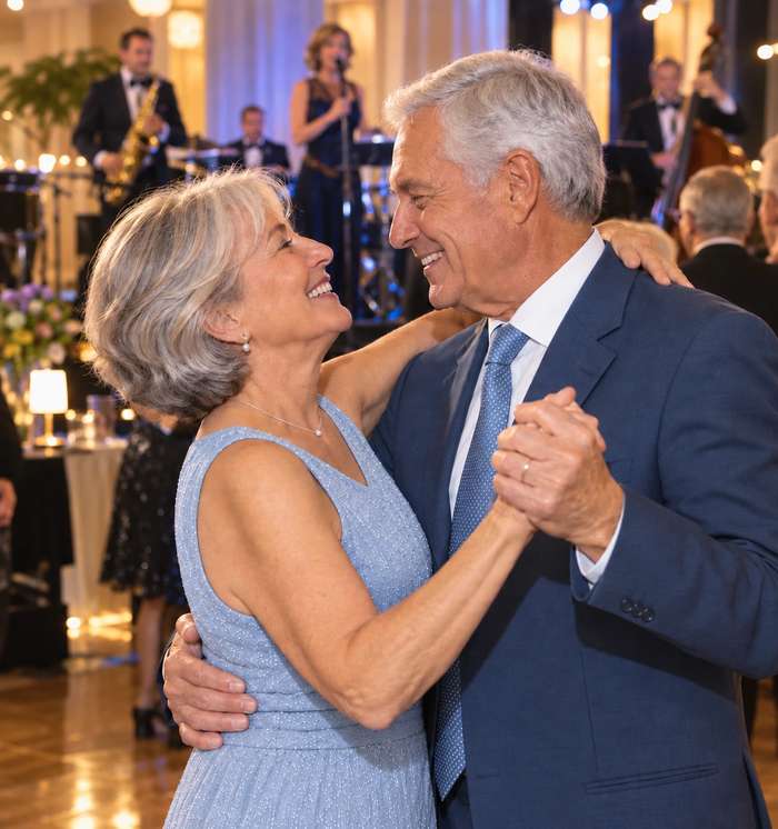 Pareja de adultos mayores bailando sonrientes en una fiesta elegante, representando el envejecimiento activo y saludable